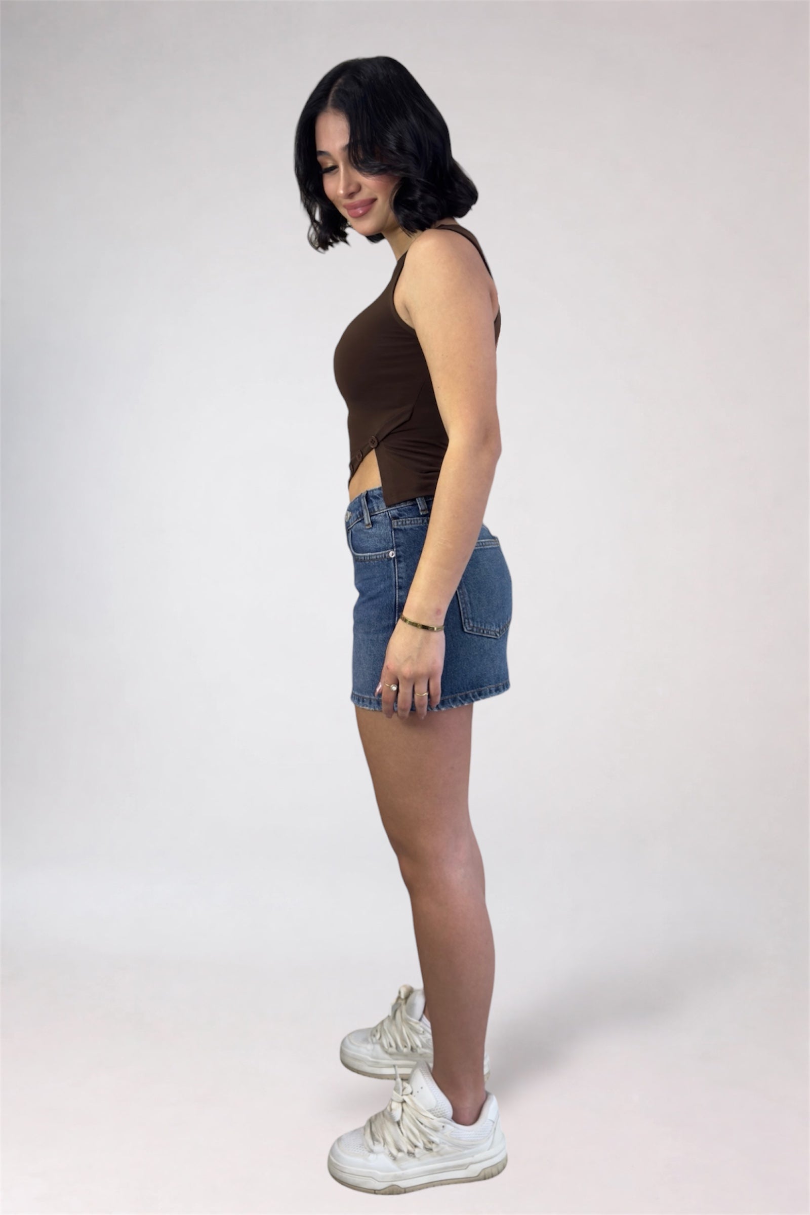Woman wearing a brown sleeveless top and denim shorts on a white background