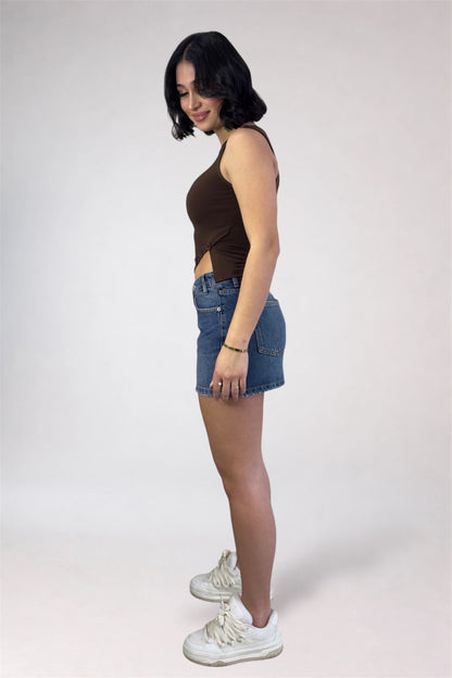 Woman wearing a brown sleeveless top and denim shorts on a white background
