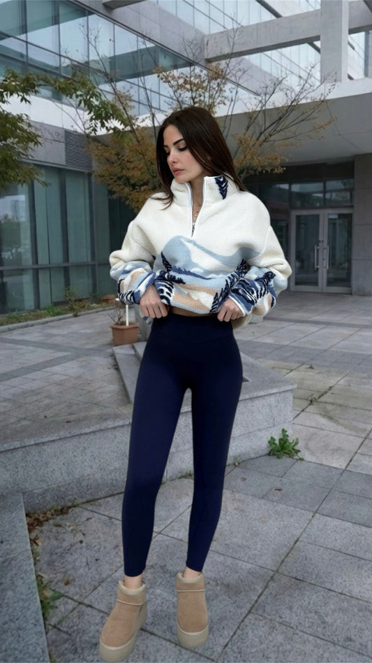 Woman wearing a white jacket and dark blue leggings standing in an outdoor setting.