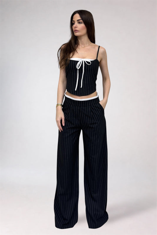 Woman wearing a black pinstripe outfit with a white top on a plain background