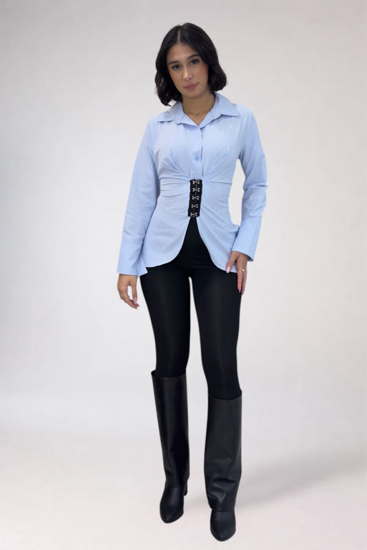Woman wearing a light blue shirt and black pants with high boots on a white background