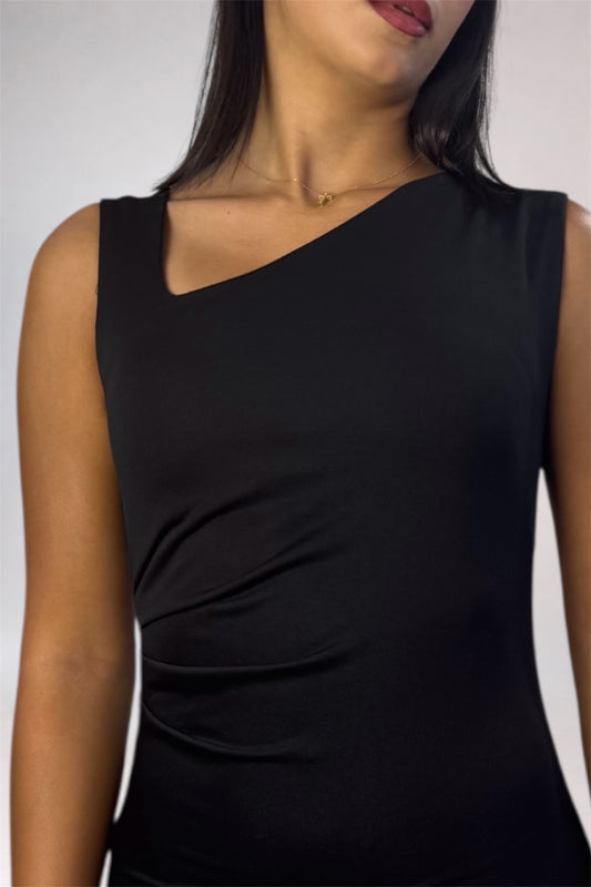A close-up of a woman wearing a black sleeveless top with an asymmetrical diagonal neckline and gathered side detailing, shown against a plain light gray background.