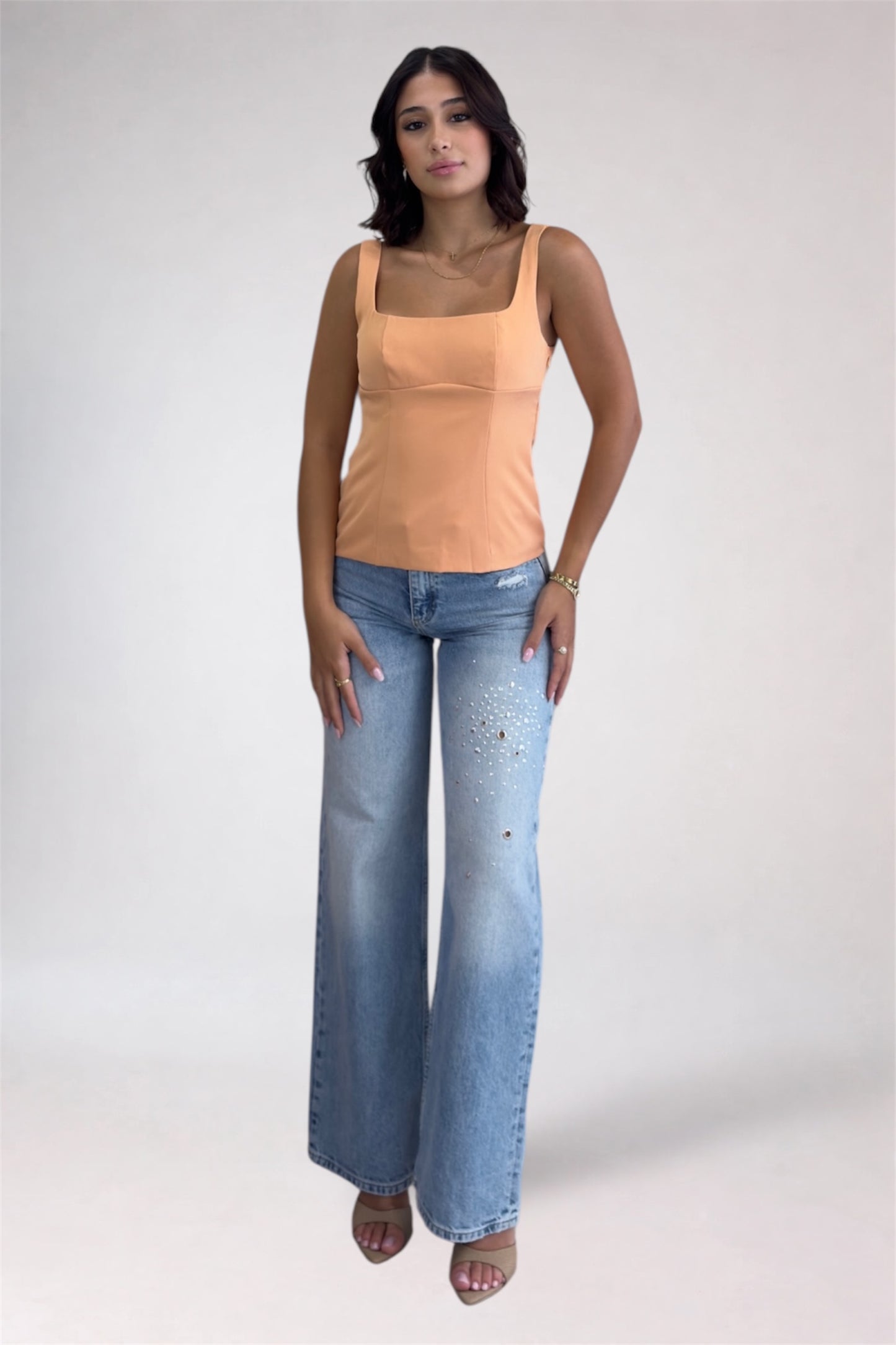 Woman wearing a peach tank top and light blue jeans on a white background