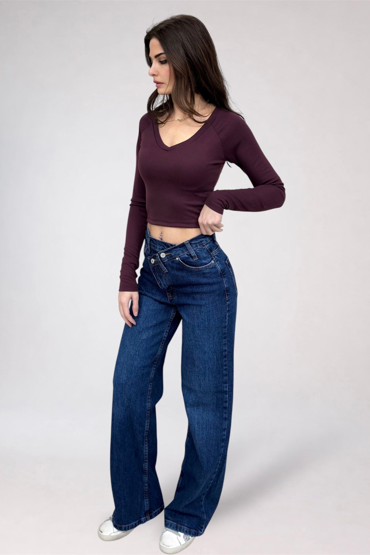 Woman wearing a burgundy long-sleeve top and blue jeans on a white background