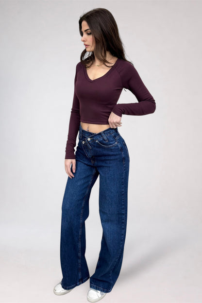Woman wearing a burgundy long-sleeve top and blue jeans on a white background