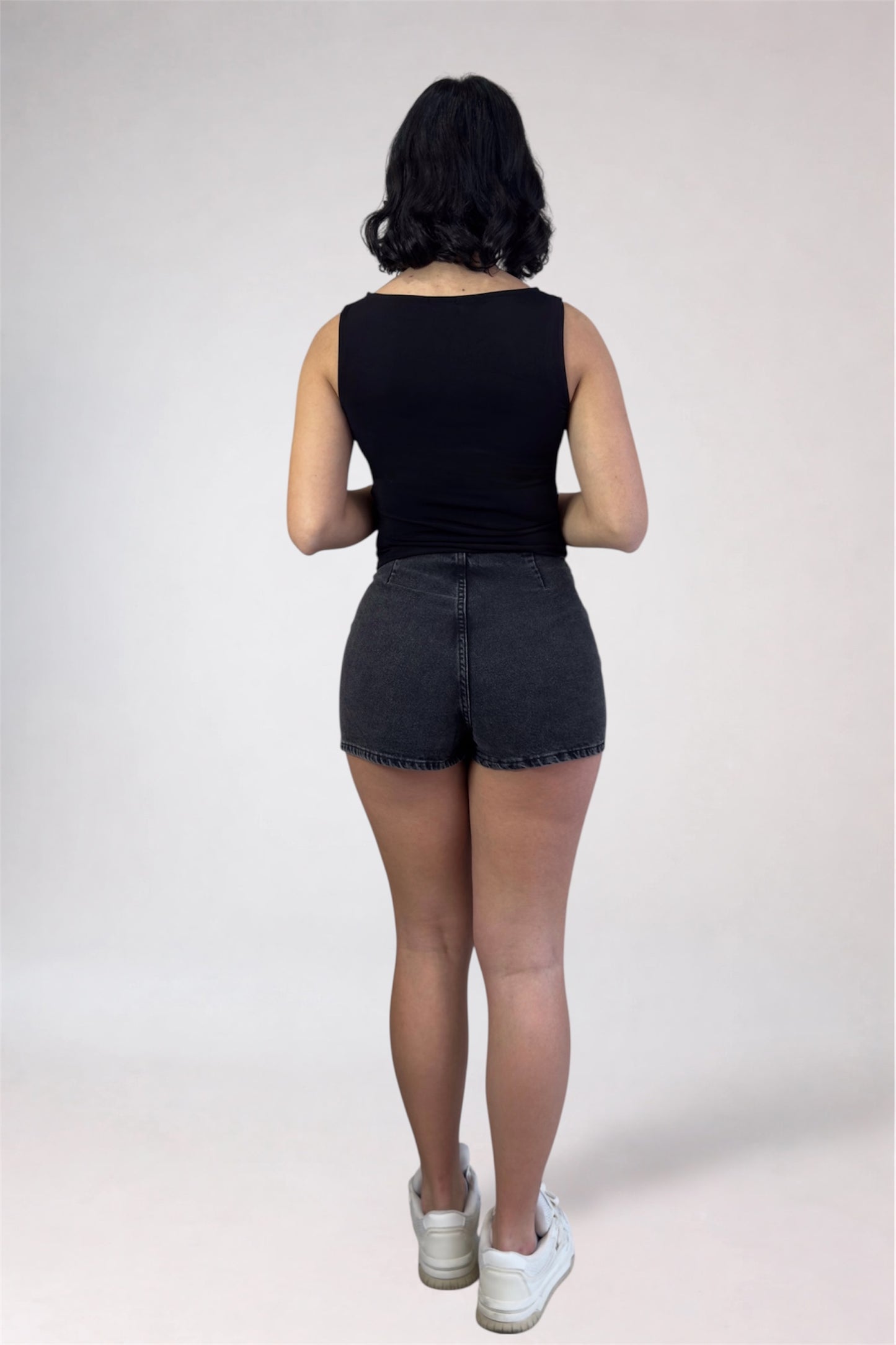 Person wearing a black sleeveless top and denim shorts on a white background
