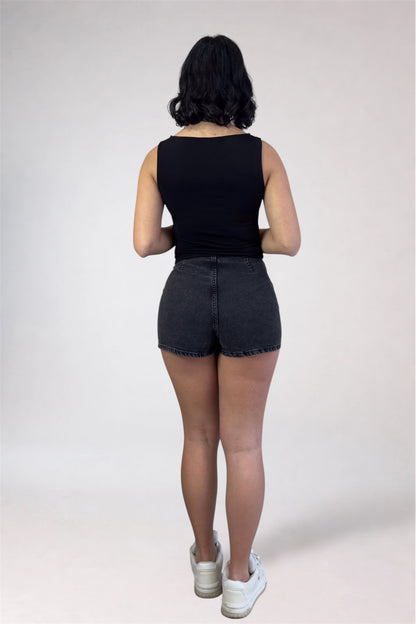 Person wearing a black sleeveless top and denim shorts on a white background