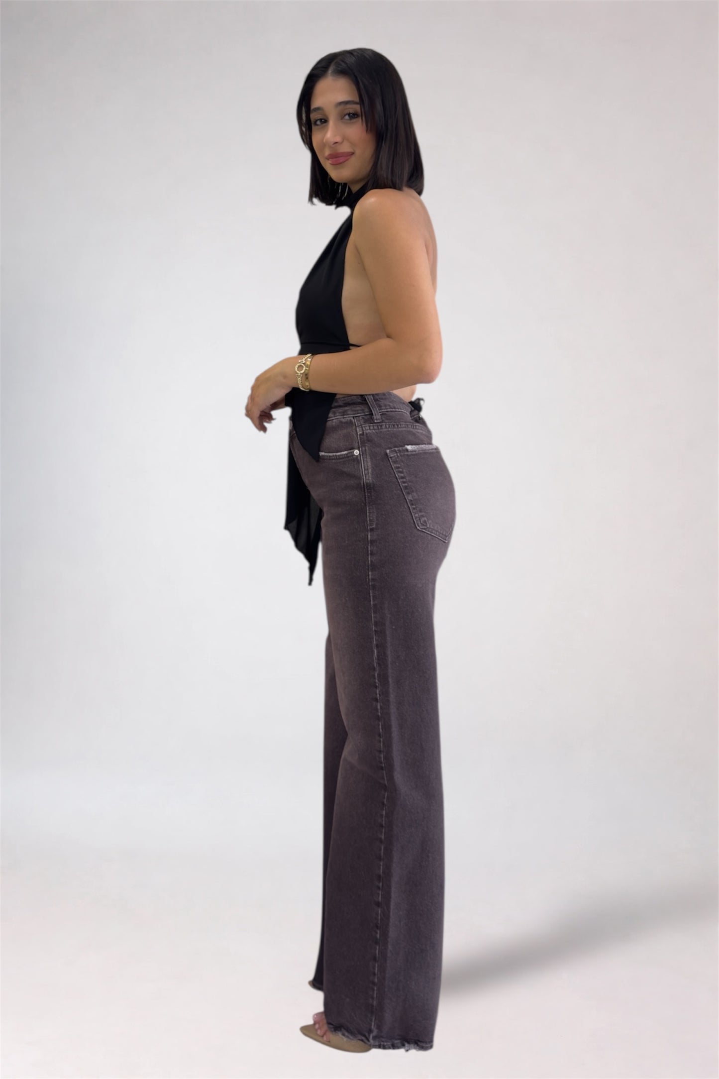 Woman wearing a black sleeveless top and gray flared jeans on a white background
