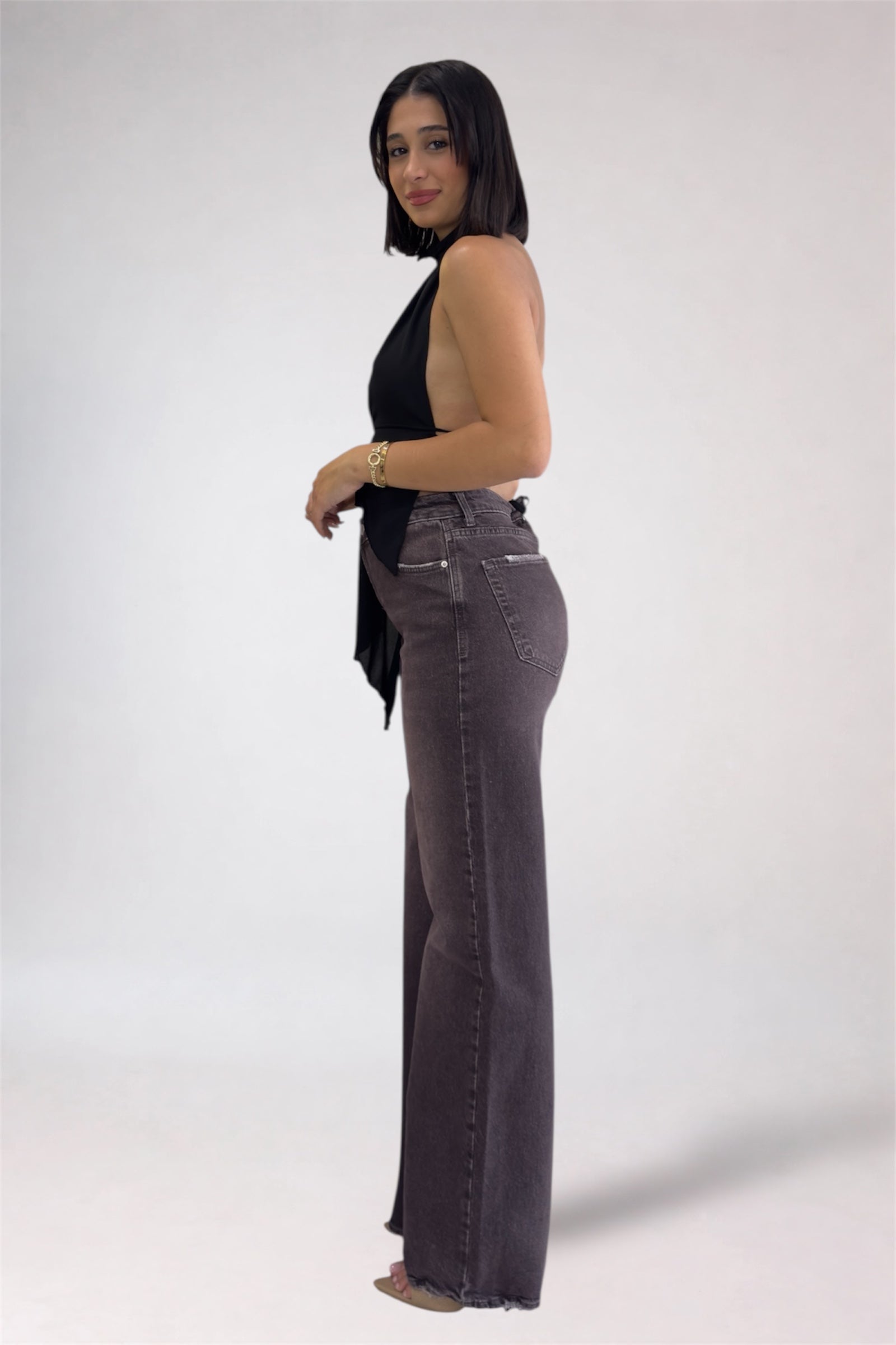Woman wearing a black sleeveless top and gray flared jeans on a white background
