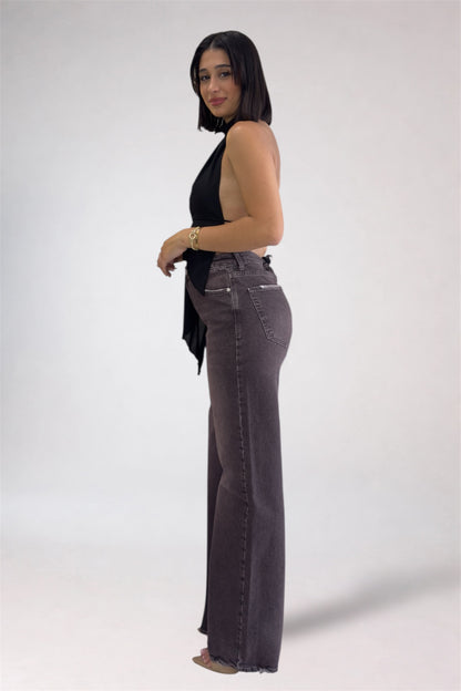 Woman wearing a black sleeveless top and gray flared jeans on a white background