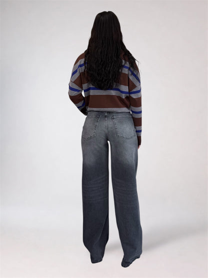 A model shown from the back wearing a brown, blue, and white striped long-sleeve top and wide-leg faded blue jeans against a light gray studio background.