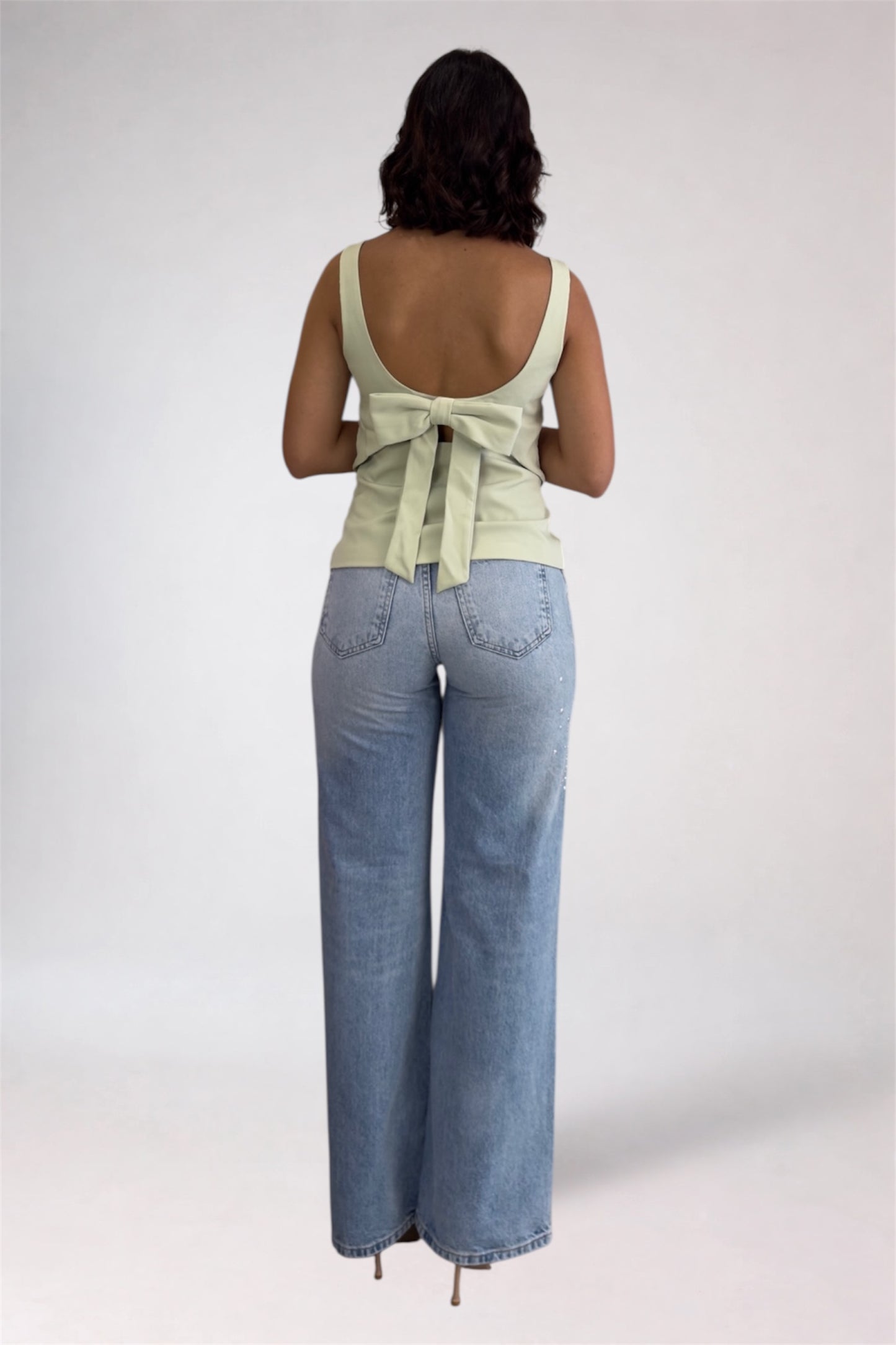 Woman wearing a light green sleeveless top and blue jeans on a plain background