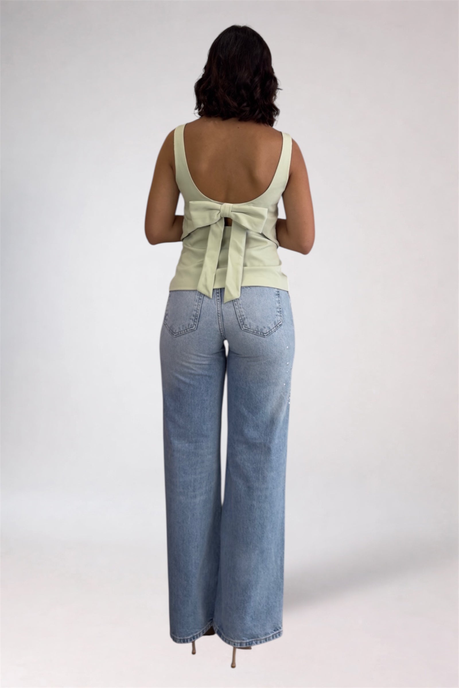 Woman wearing a light green sleeveless top and blue jeans on a plain background