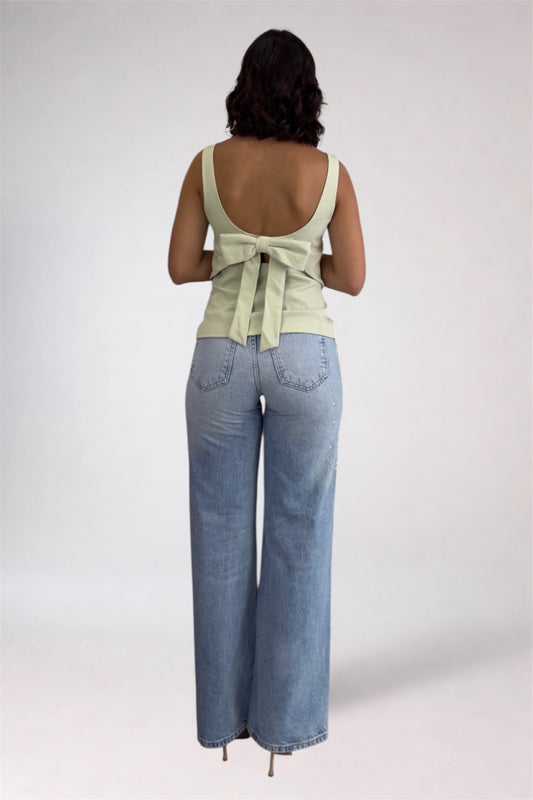 Woman wearing a light green sleeveless top and blue jeans on a plain background