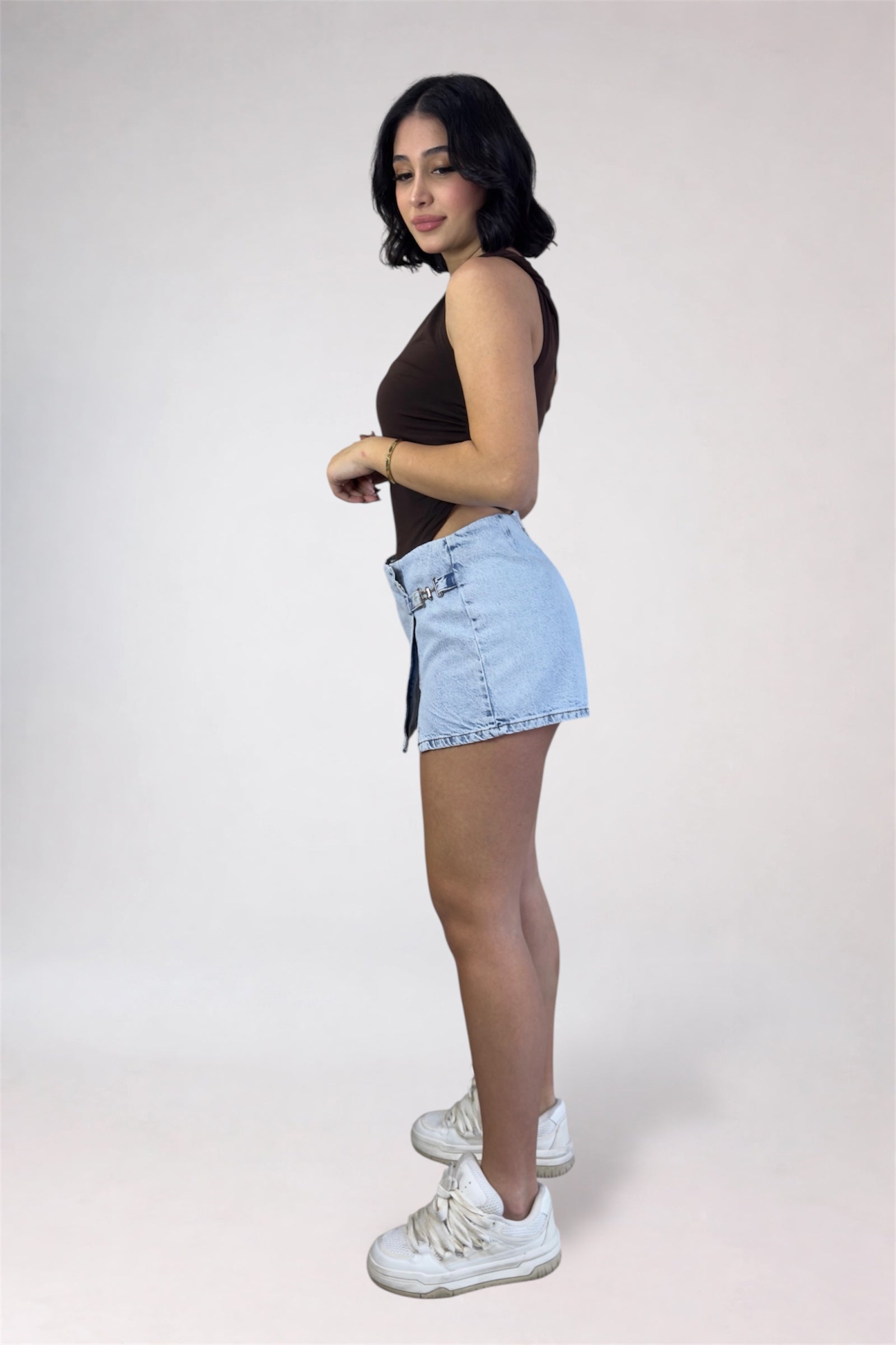 Woman wearing a black sleeveless top and light blue denim shorts on a white background