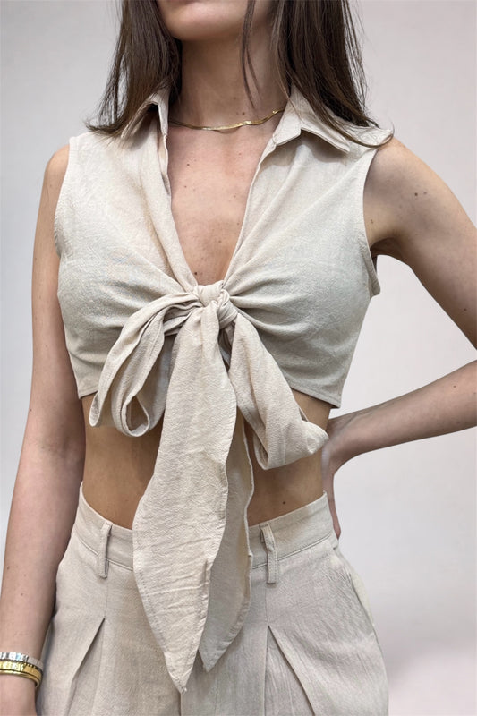 Woman wearing a beige sleeveless top with a knot detail and matching pants on a plain background