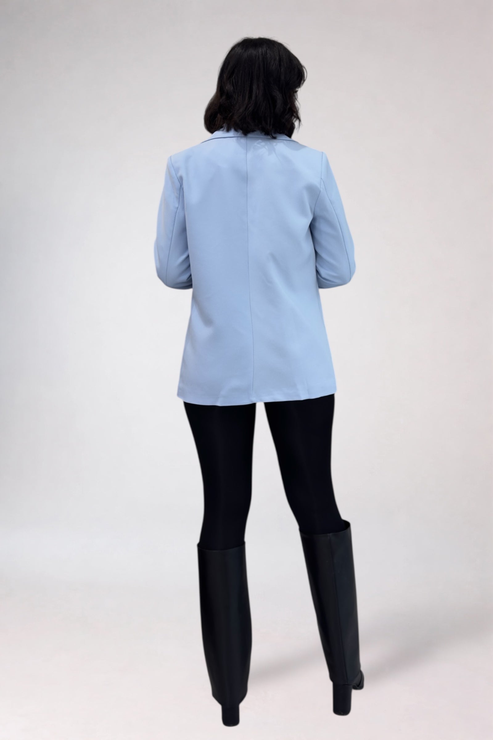 Person wearing a light blue jacket, black pants, and black boots on a white background