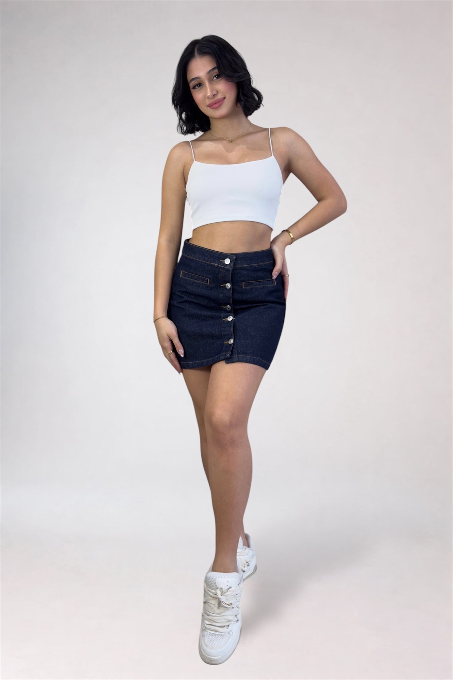 Woman wearing a white top and dark denim skirt on a plain background