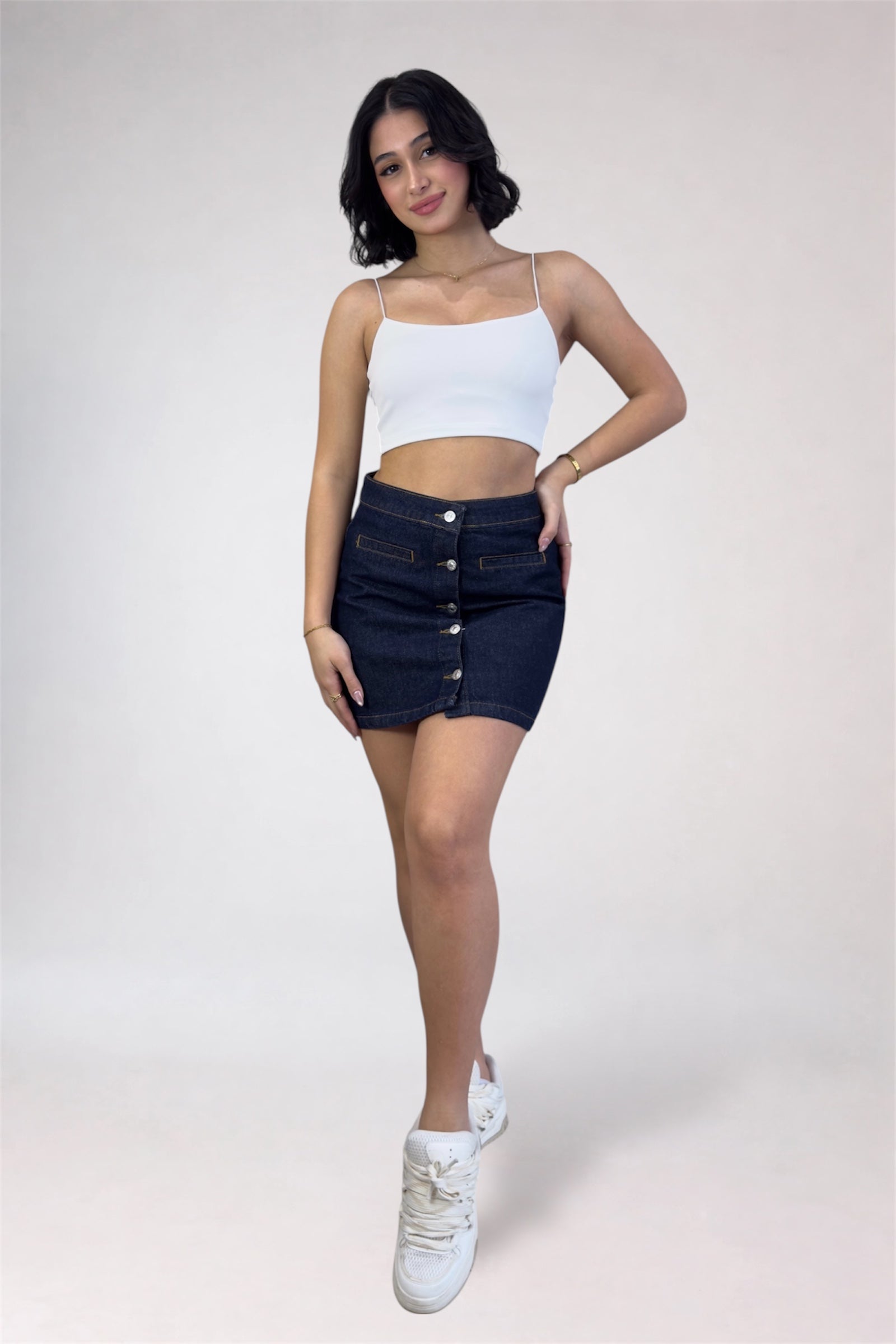 Woman wearing a white top and dark denim skirt on a plain background