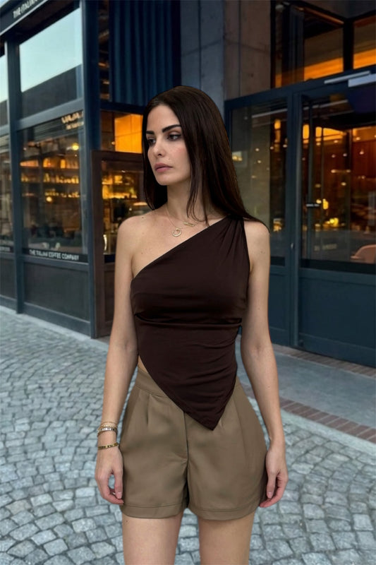 Woman wearing a brown one-shoulder top and beige shorts standing on a street.