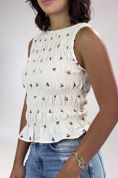 Woman wearing a white sleeveless top with red cherry pattern and blue jeans on a plain background