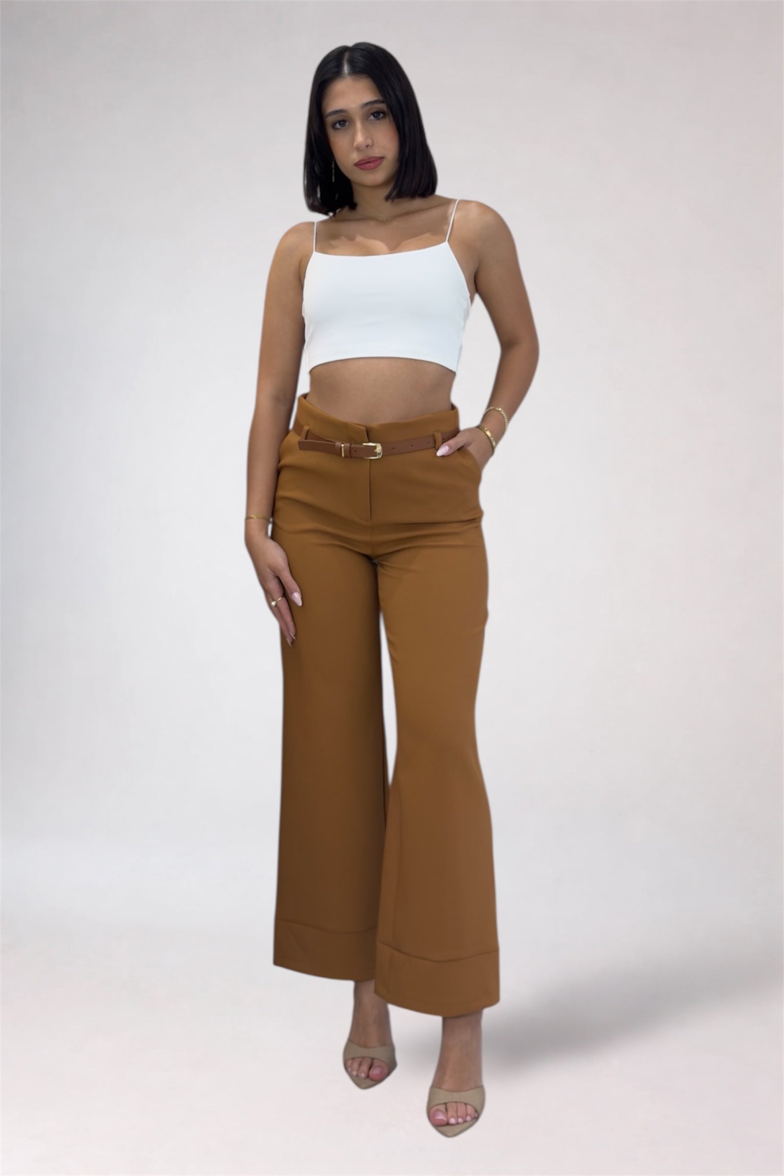 Woman wearing a white top and brown high-waisted pants on a plain background