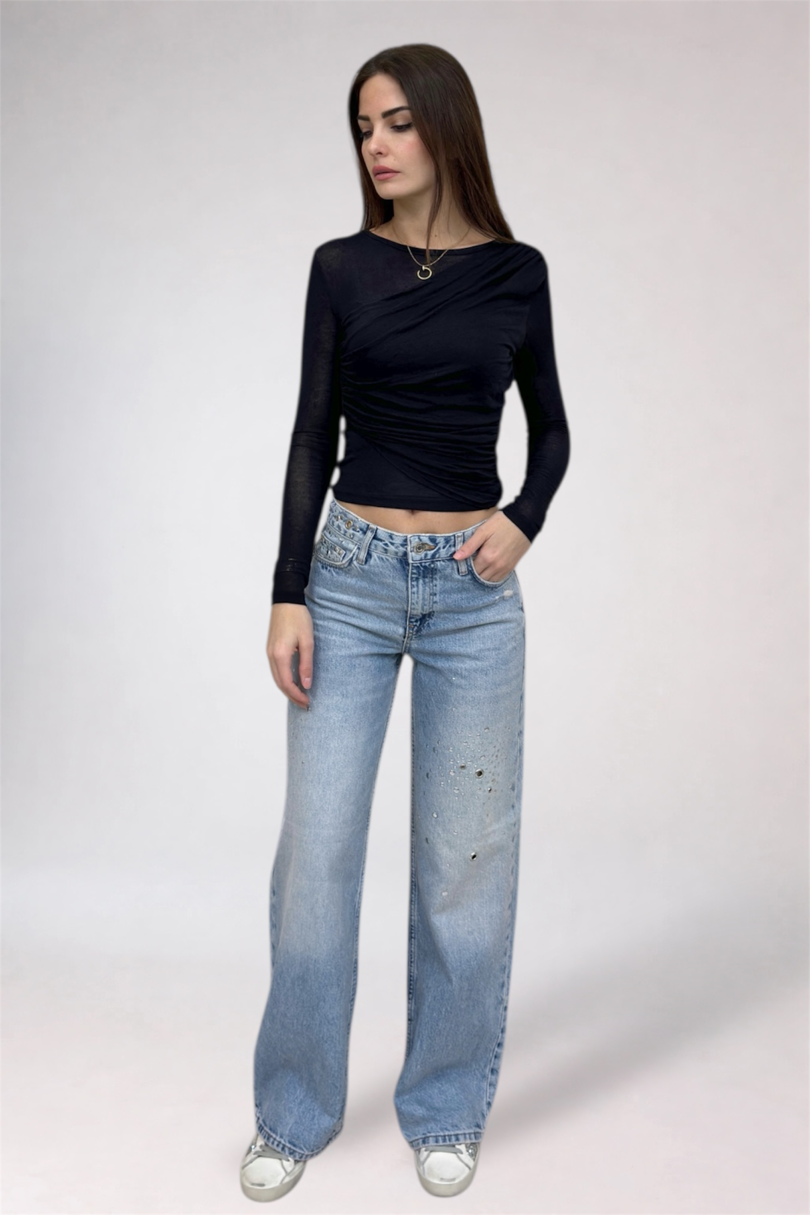 Woman wearing a black long-sleeve top and light blue jeans on a white background