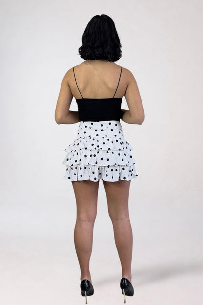Person wearing a black top and white polka dot skirt on a plain background