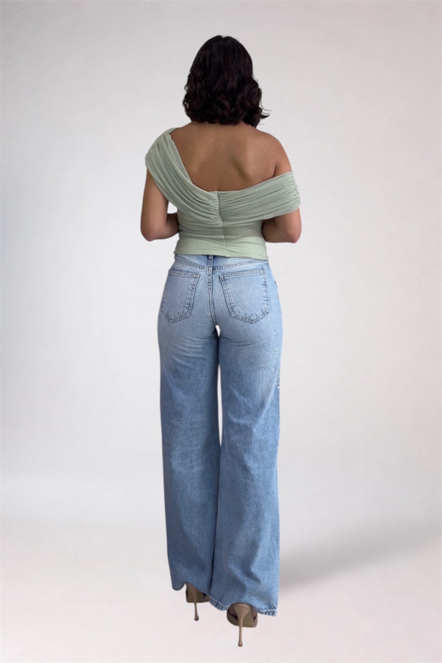 Person wearing a light green off-shoulder top and blue jeans on a white background