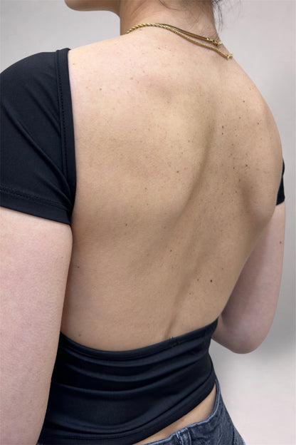 Person wearing a black sleeveless top with an open back, showing a necklace.