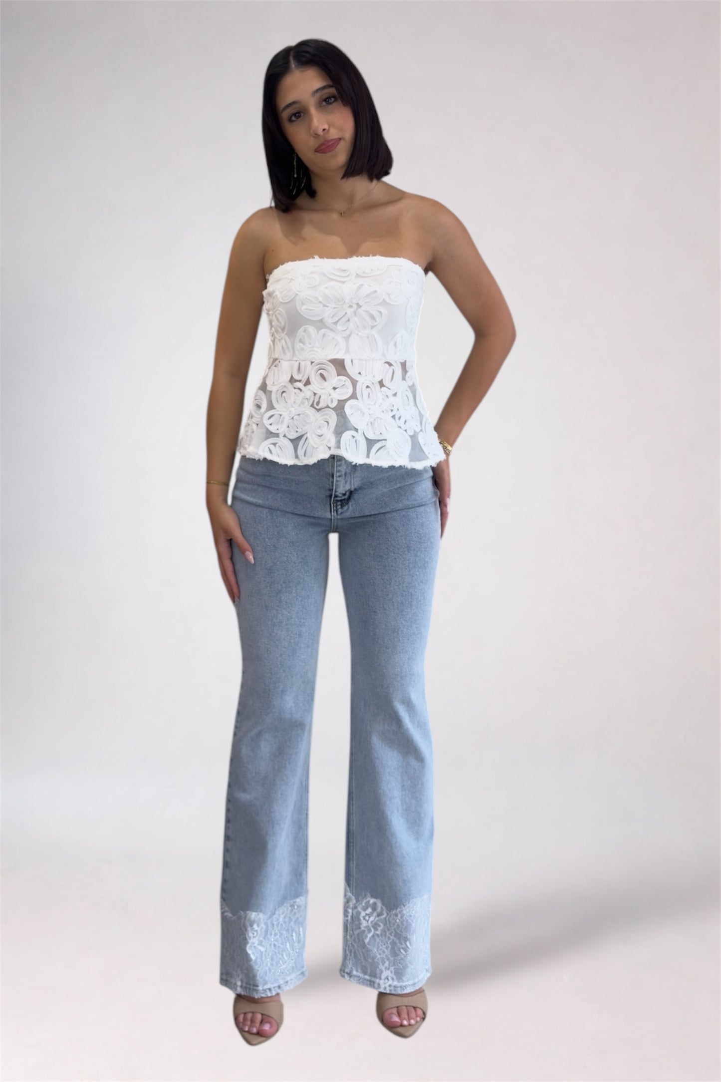 Woman wearing a white lace top and light blue jeans on a white background