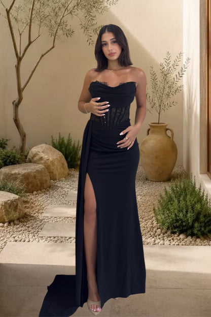 Woman in a black strapless gown with a high slit standing outdoors.