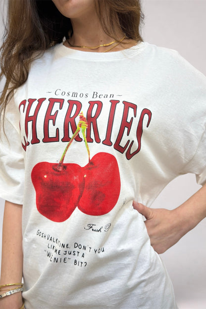 Person wearing a white t-shirt with red cherries and text design.