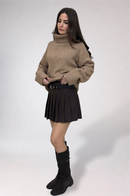 Woman wearing a beige sweater, black pleated skirt, and black boots on a white background