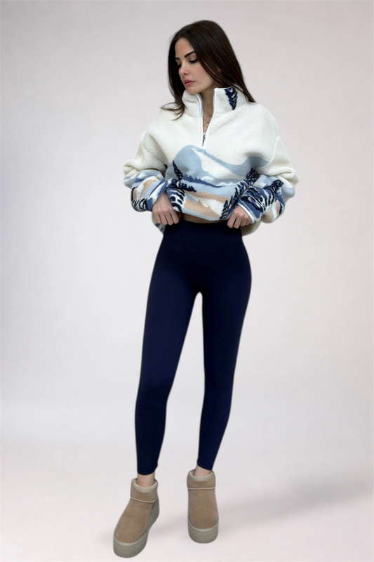 Woman wearing a patterned sweater, navy leggings, and tan boots on a white background