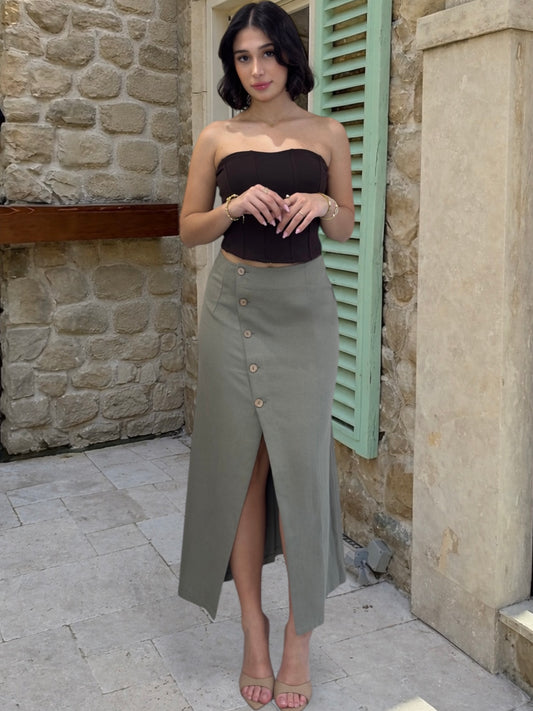 Woman wearing a black top and green skirt standing against a stone wall.