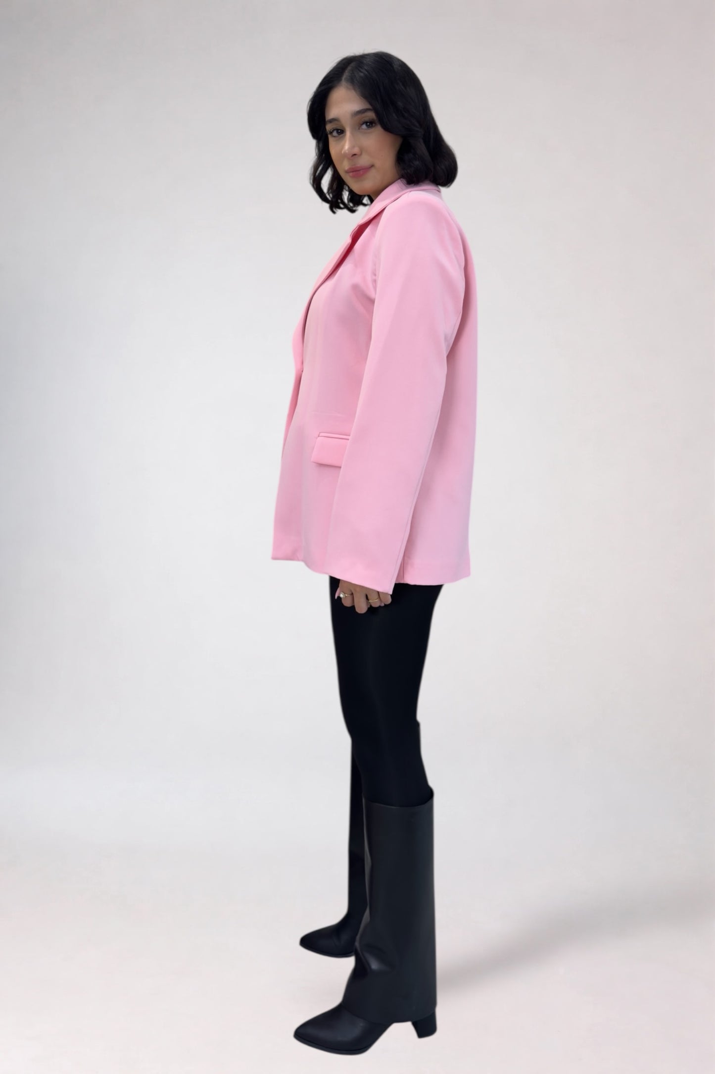 Person wearing a pink blazer, black pants, and black knee-high boots on a white background
