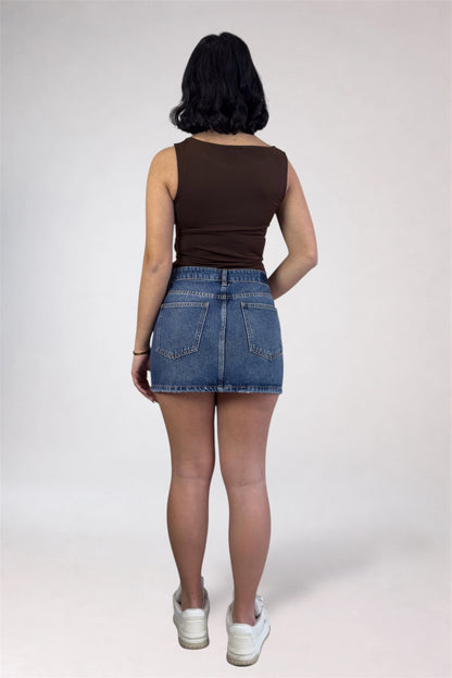 Person wearing a brown tank top and denim skirt on a white background