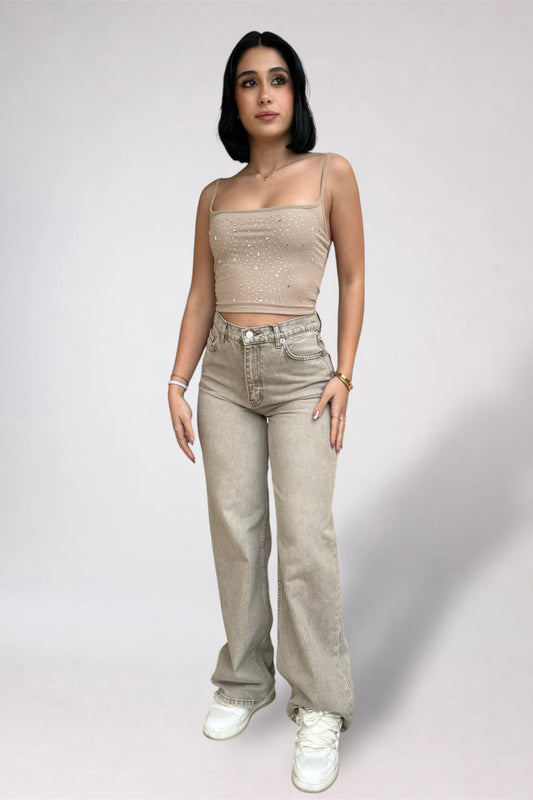 Woman wearing a beige top and light-colored pants on a plain background