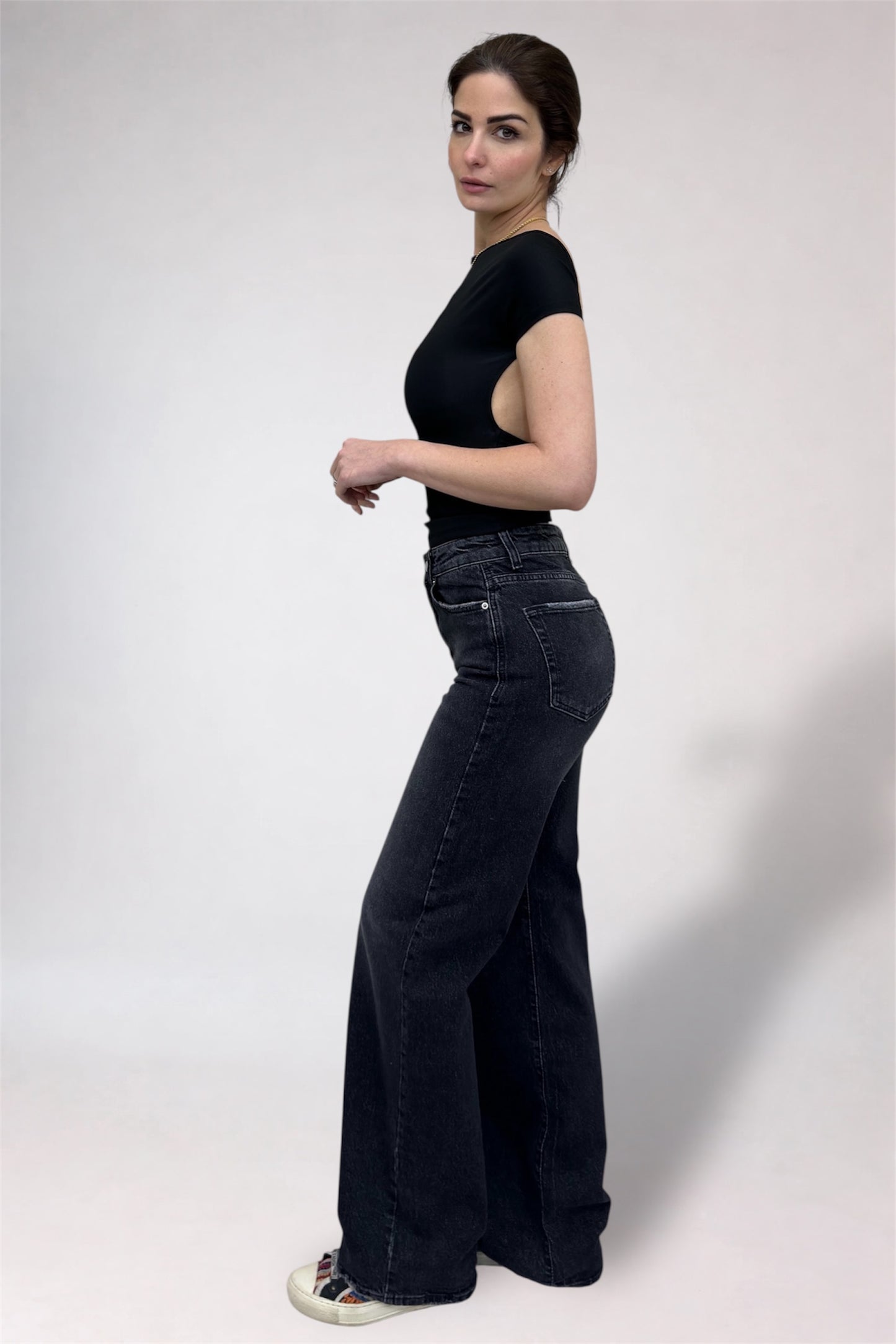 Woman wearing black high-waisted jeans and a black top on a white background