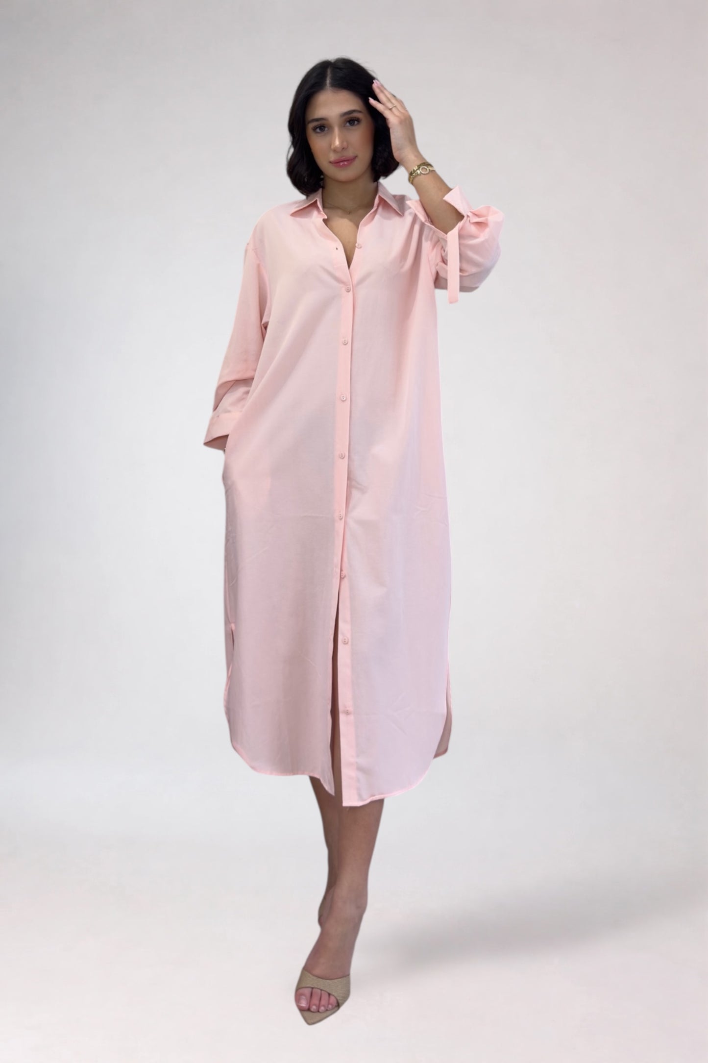 Woman wearing a light pink shirt dress against a white background