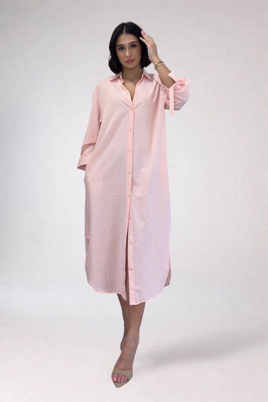 Woman wearing a light pink shirt dress against a white background