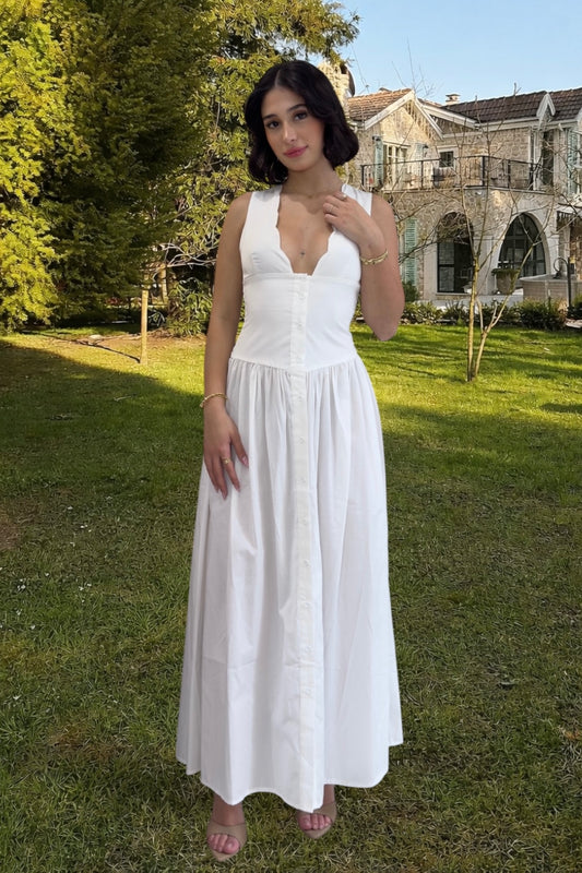 Woman in a white dress standing in a grassy area with trees and a building in the background
