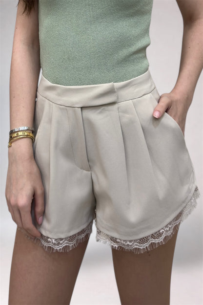 Person wearing beige shorts with lace trim on a plain background
