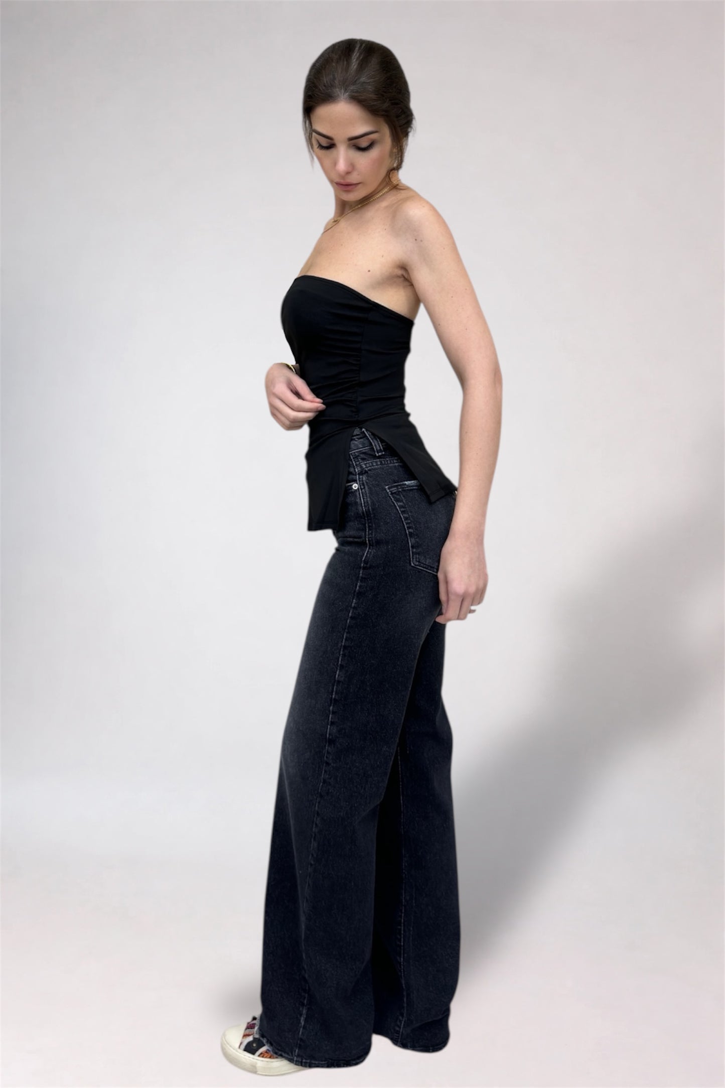 Woman wearing a black strapless top and wide-leg jeans on a white background