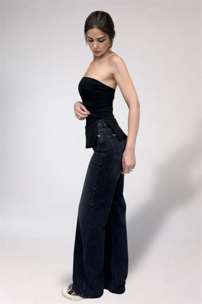 Woman wearing a black strapless top and wide-leg jeans on a white background