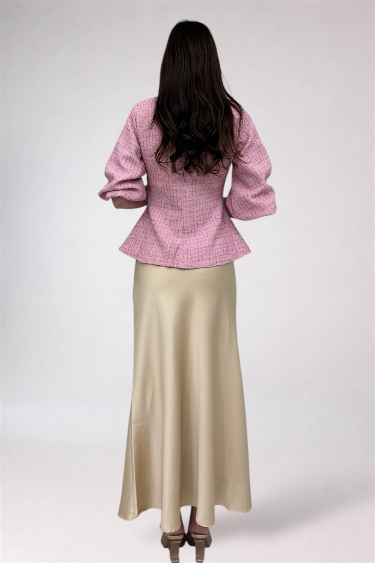 Woman wearing a pink checkered jacket and beige skirt on a white background