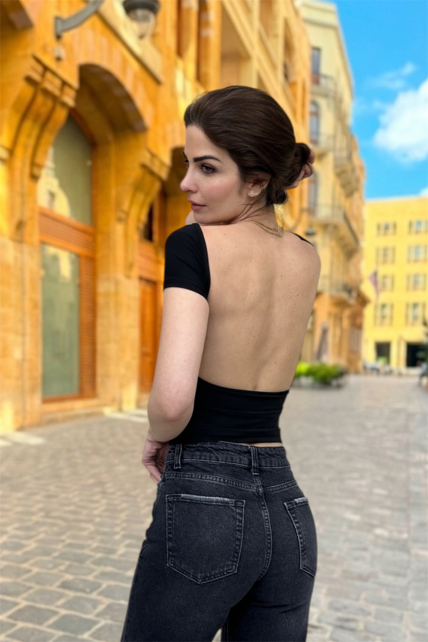 Woman in a black outfit standing on a street with yellow buildings in the background