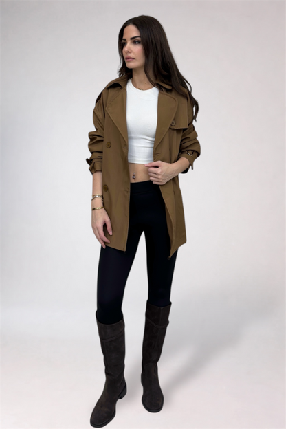 Woman wearing a brown coat, white top, black pants, and dark boots on a white background