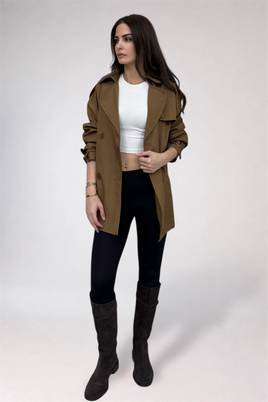 Woman wearing a brown coat, white top, black pants, and dark boots on a white background